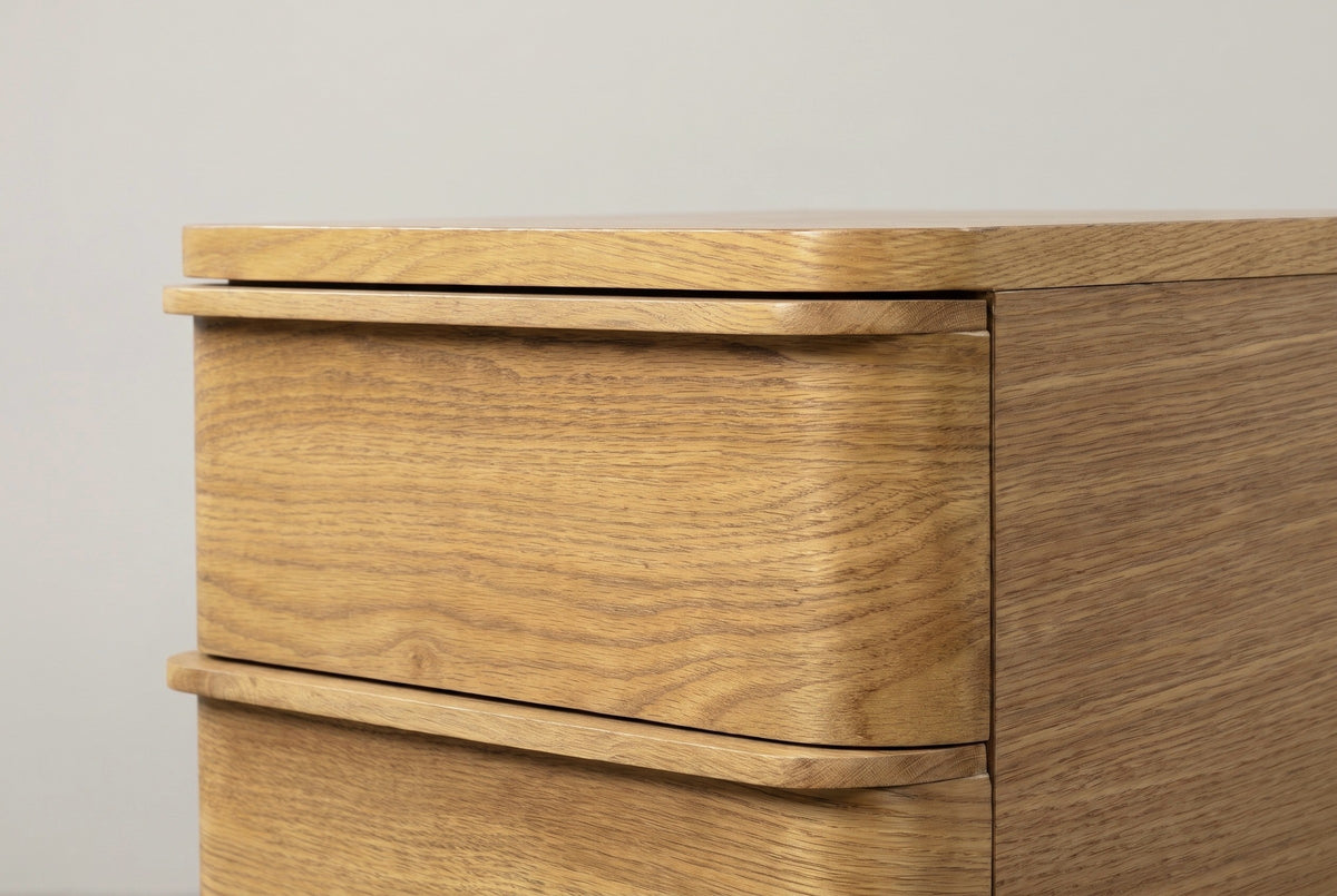 The top drawer of the Arzachena nightstand: its front curving back around the corner under the rounded top, with the thin oak lip that serves as the pull