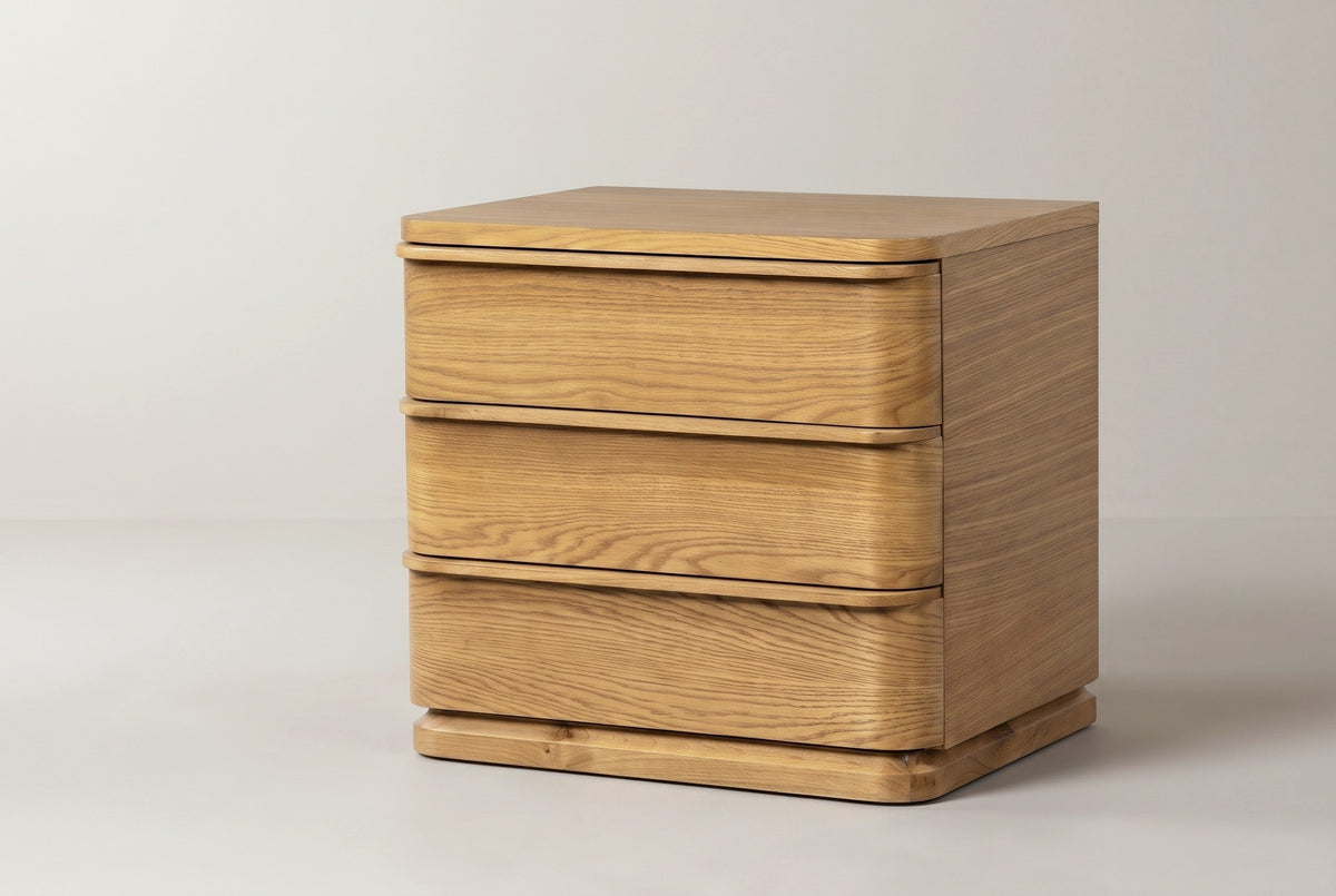 The Arzachena three-drawer nightstand in natural oak, three-quarter view on a light studio backdrop