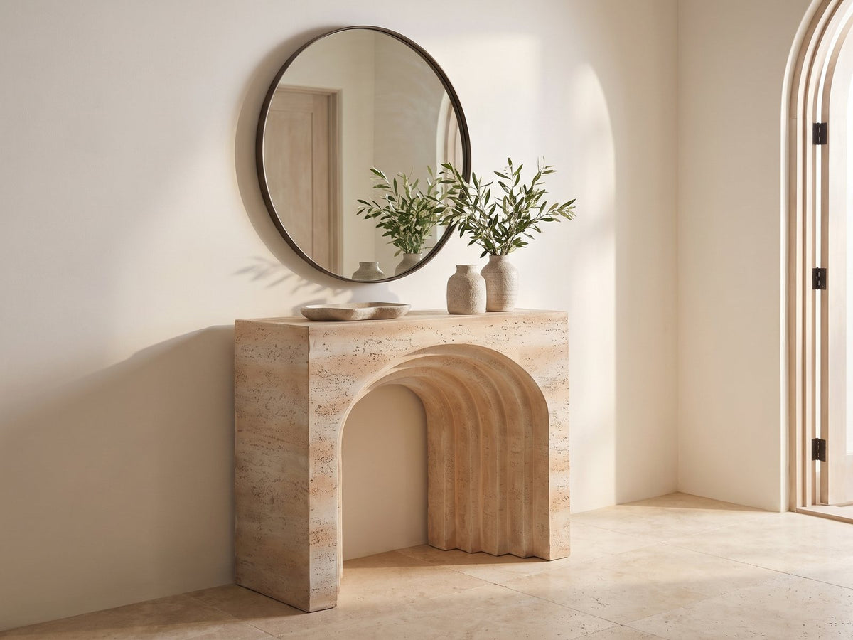 Asiago Faux Travertine Arched Console Table under a round mirror beside a tall arched glass door in a travertine entryway