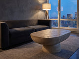 Asiago Faux Travertine Oval Mushroom Coffee Table on a wool rug in front of a velvet sofa in a city penthouse at blue hour
