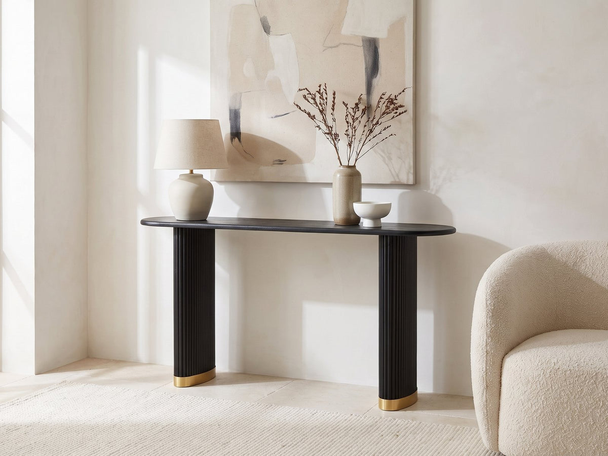 Atina Black Ash Oval Console Table against a plaster wall under an abstract canvas in a bright living room
