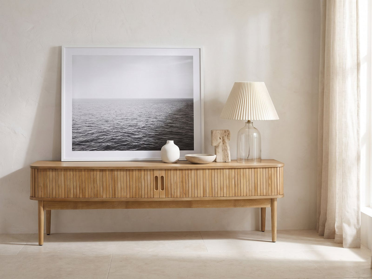Atrani Reeded Curved Media Console styled with a leaning print, a lamp and ceramics in a bright plaster room
