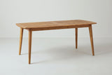 The Augusta outdoor dining table in teak-finish acacia, closed, with a slatted top in two framed halves and four tapered legs, three-quarter view on a light studio backdrop