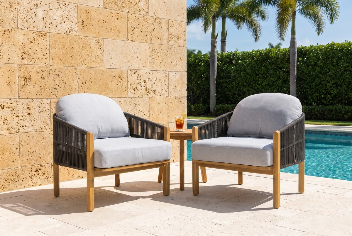 Two Avola club chairs on a travertine pool deck in Naples, Florida, a honey keystone coral-stone wall, palms and a clipped hedge behind (side table not included)