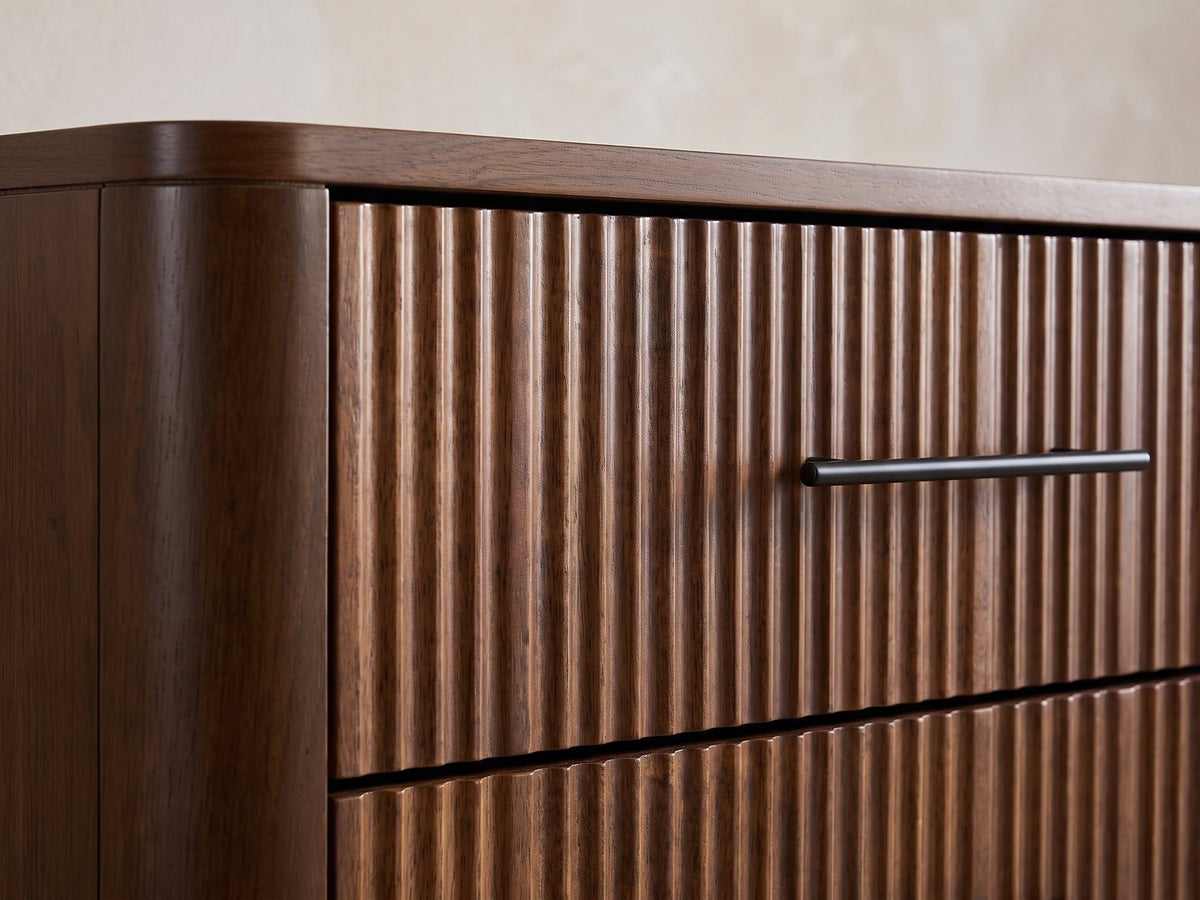 Close-up of the Badia 56-Inch Walnut-Finish 6-Drawer Dresser: a reeded drawer front with its slim black bar pull beside the rounded end of the case