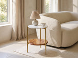 Badolato Marble and Acacia Two-Tier Side Table with a lamp and a ceramic bowl beside a curved cream boucle seat in a bright plaster room