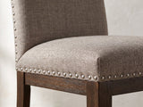 Close-up of the Bagnara 76.5 to 94.5-Inch Rustic Oak Double Pedestal Dining Set with 4 Chairs: the taupe linen-look seat, pewter nailheads and dark brown seat rail of a chair