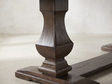 Close-up of the Bagnara 76.5 to 94.5-Inch Rustic Oak Double Pedestal Dining Set with 4 Chairs: the square urn-shaped baluster pedestal and its moulded foot