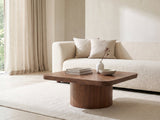 Bari Walnut Veneer Square Pedestal Coffee Table styled with books, a vase and a stone bowl in front of a cream sofa in a bright plaster room