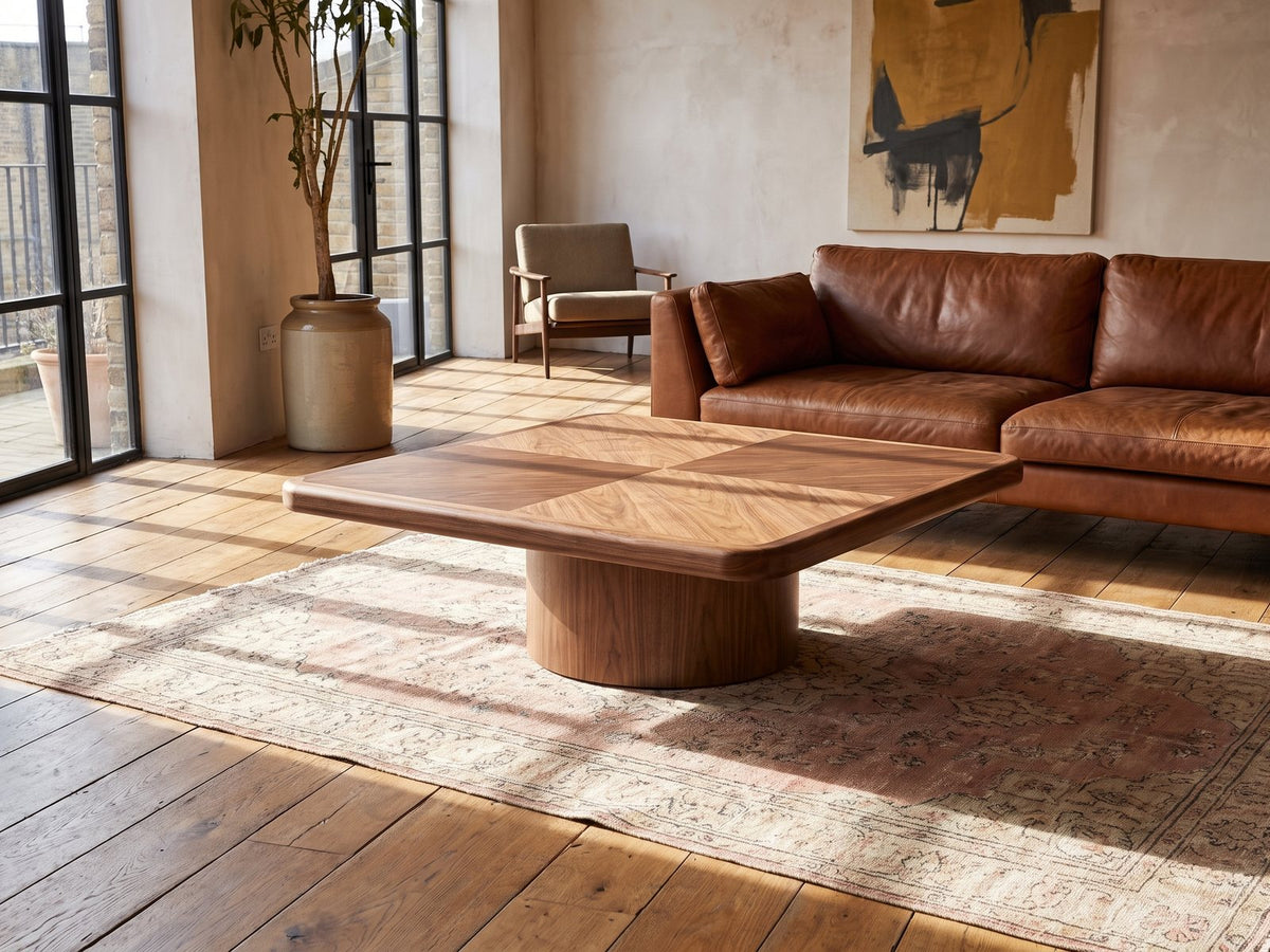 Bari Walnut Veneer Square Pedestal Coffee Table seen from the side, on a vintage rug in front of a leather sofa in an industrial loft