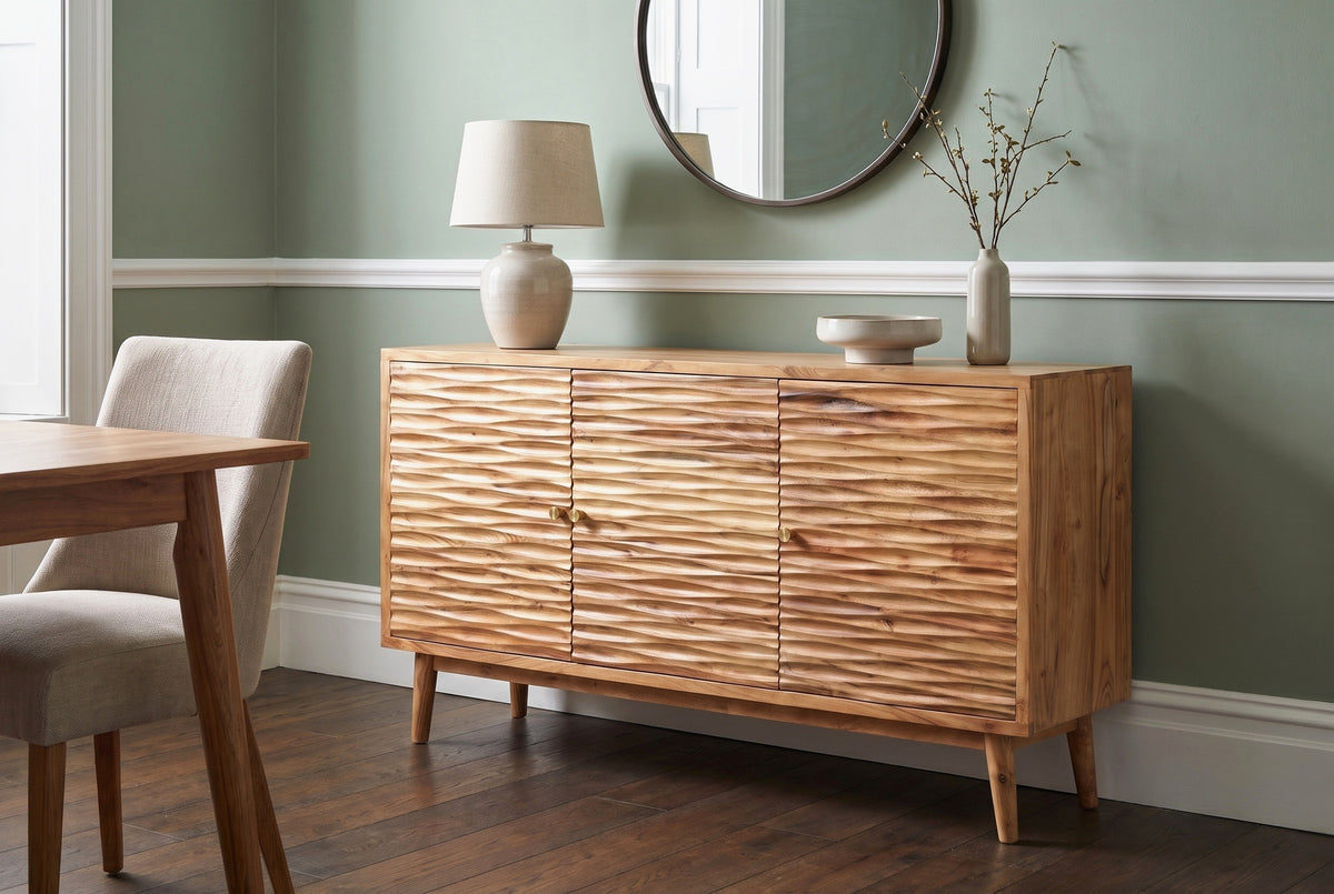 Barile carved sideboard with a lamp, a bowl and a vase under a round mirror against a sage-green wall with a white picture rail in a Charleston dining room