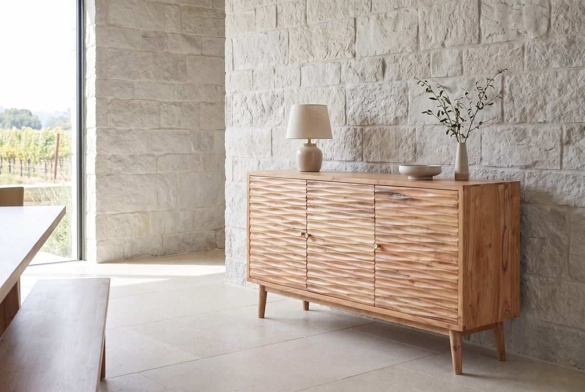 Barile carved three-door sideboard with a lamp, a bowl and a vase on top, against a pale limestone wall in a Napa Valley dining room with a tall window and a stone floor