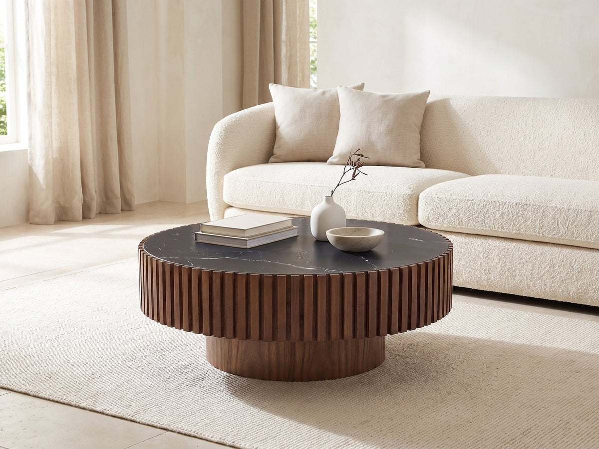 Barolo 35-Inch Round Black Sintered Stone Slatted Drum Coffee Table styled with books, a vase and a stone bowl in front of a cream sofa in a bright plaster room
