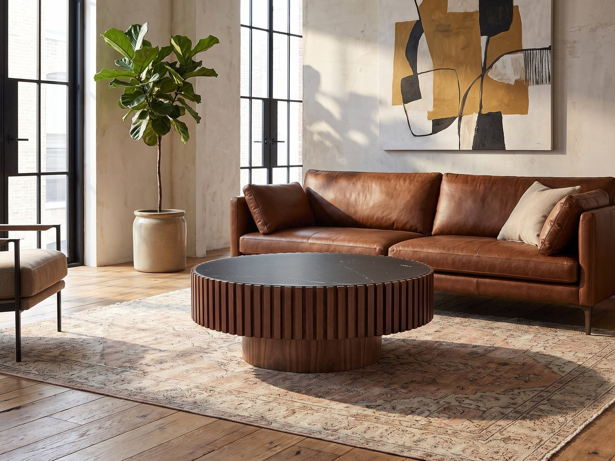 Barolo 35-Inch Round Black Sintered Stone Slatted Drum Coffee Table seen from the side, on a vintage rug in front of a leather sofa in an industrial loft