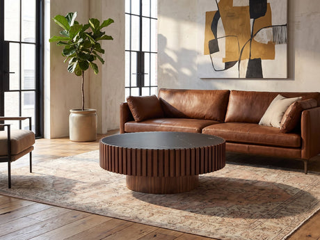 Barolo 35-Inch Round Black Sintered Stone Slatted Drum Coffee Table seen from the side, on a vintage rug in front of a leather sofa in an industrial loft