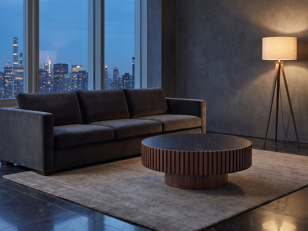 Barolo 35-Inch Round Black Sintered Stone Slatted Drum Coffee Table on a wool rug in front of a velvet sofa in a city penthouse at blue hour