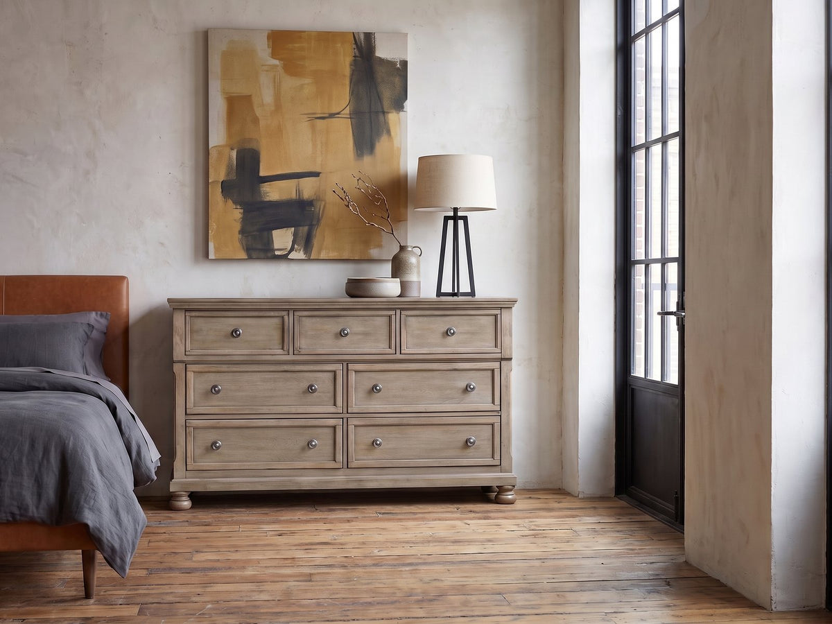 Bassano 65-Inch Wire-Brushed Driftwood Gray 7-Drawer Dresser against a plaster wall in an industrial loft bedroom
