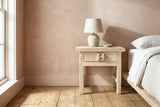 Baunei reclaimed elm nightstand with a ceramic lamp beside a low bed in a Nashville farmhouse bedroom with a dusty terracotta wall and a tall window