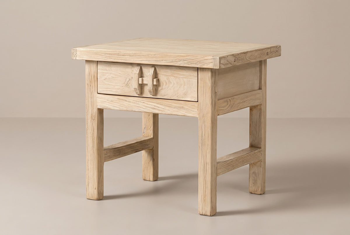 The Baunei one-drawer nightstand in pale reclaimed elm with a carved wooden pull, three-quarter view on a light studio backdrop