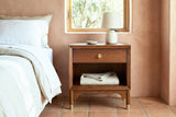 Berchidda walnut nightstand with a ceramic lamp beside a bed in an Ojai bedroom with terracotta plaster walls and a terracotta tile floor