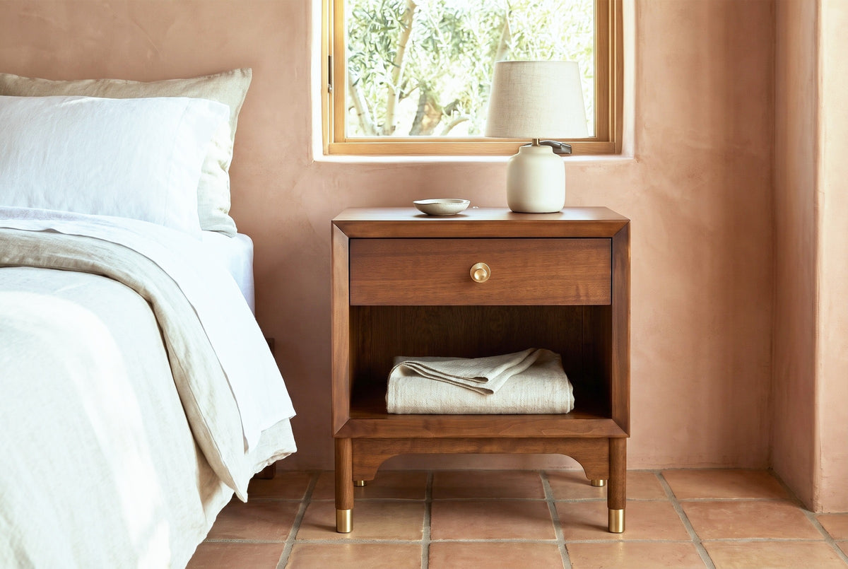 Berchidda walnut nightstand with a ceramic lamp beside a bed in an Ojai bedroom with terracotta plaster walls and a terracotta tile floor