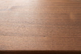 Close-up of the walnut veneer on the Berchidda nightstand: fine, straight grain in a warm medium brown running to the edge of the top