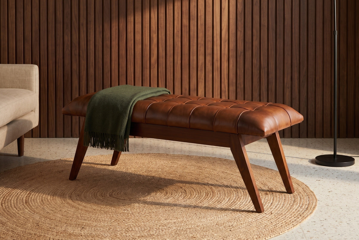 Bevagna cognac leather bench against a wall of dark walnut slats in a Los Angeles living room with a terrazzo floor, a round jute rug and a green wool throw