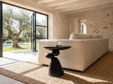 Bitetto Black Fiberglass Stacked Pebble Side Table beside a linen sofa in a poolside villa