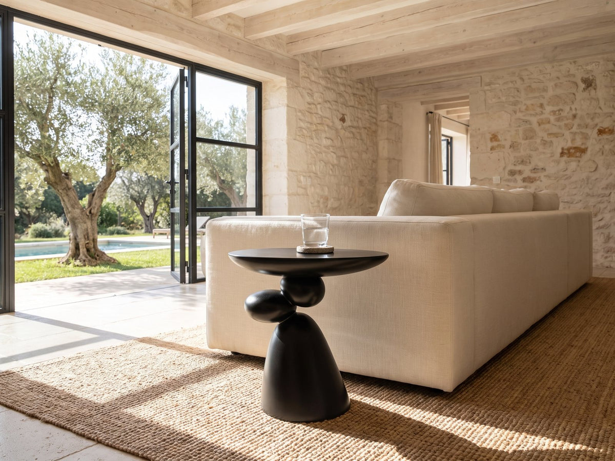 Bitetto Black Fiberglass Stacked Pebble Side Table beside a linen sofa in a poolside villa