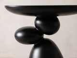 Close-up of the Bitetto Black Fiberglass Stacked Pebble Side Table: the two black pebbles balanced between the oval top and the cone
