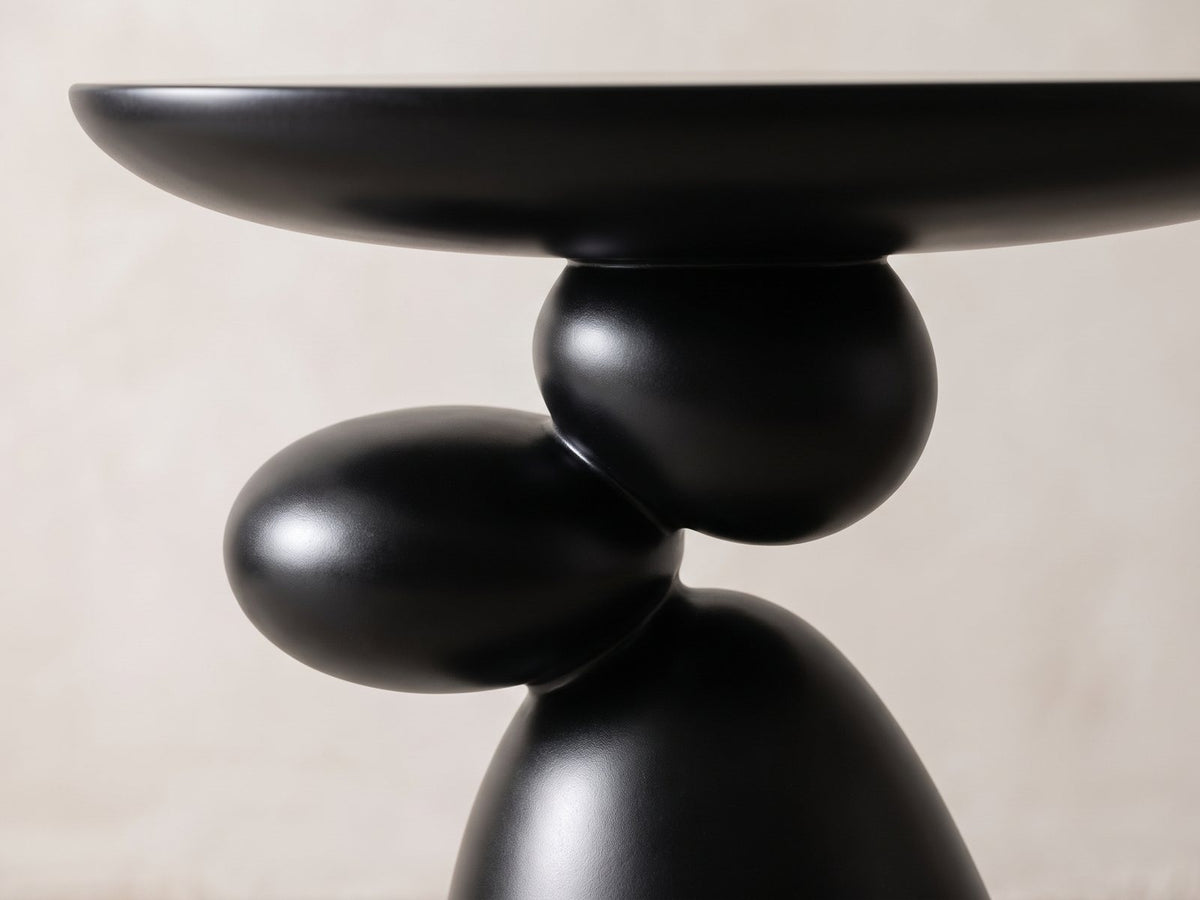 Close-up of the Bitetto Black Fiberglass Stacked Pebble Side Table: the two black pebbles balanced between the oval top and the cone