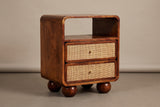 The Bitti nightstand in chestnut mango with an open cubby, two cane drawers and four round wooden feet, three-quarter view on a light studio backdrop