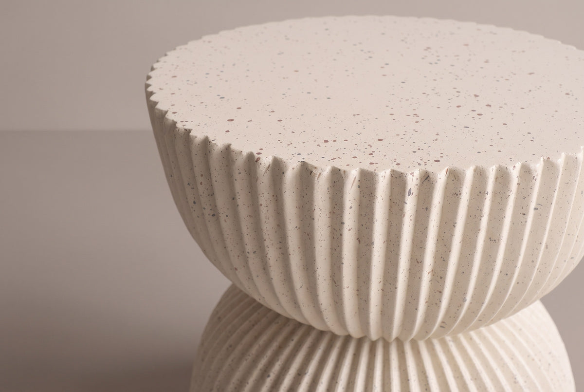Close-up of the scalloped rim and ribs of the Bivona side table in beige MGO with a hand-applied speckled finish