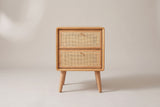 The Bono nightstand in light oak, front view on a light studio backdrop: two cane drawers with gold knobs and four splayed legs