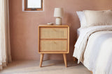 Bono oak and cane nightstand with a ceramic lamp against a dusty terracotta-pink clay plaster wall in a Tucson bedroom with a polished concrete floor