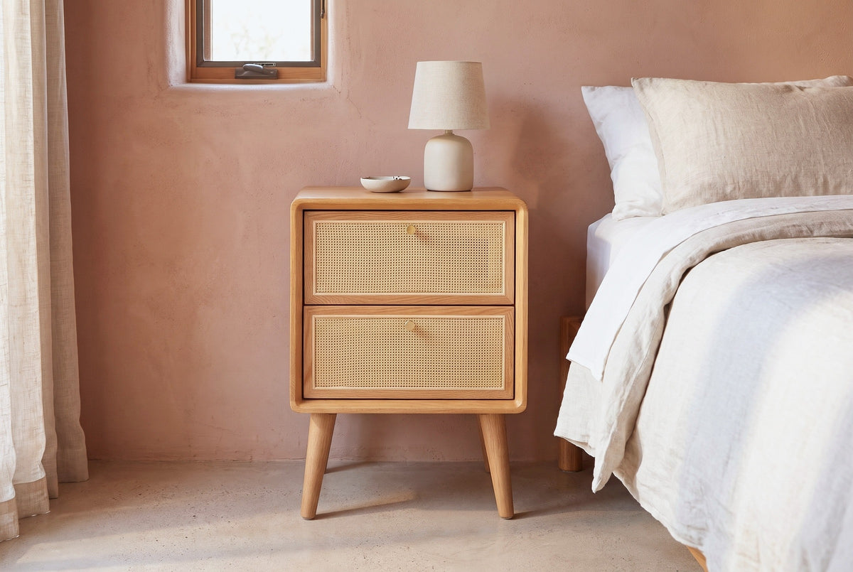 Bono oak and cane nightstand with a ceramic lamp against a dusty terracotta-pink clay plaster wall in a Tucson bedroom with a polished concrete floor