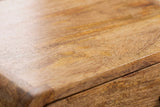 Close-up of the light mango wood on the Bonorva nightstand: warm honey grain with golden streaks running to a rounded edge