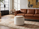 Bordighera Braided Jute and Cotton Round Pouf on a vintage rug in front of a leather sofa in an industrial loft
