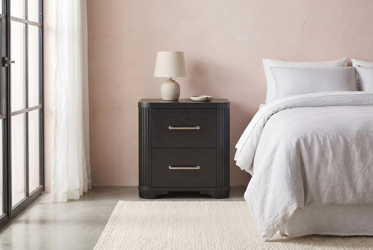 Bosa charcoal oak nightstand against a blush pink plaster wall in a Palm Springs bedroom with a polished concrete floor and a steel-framed window