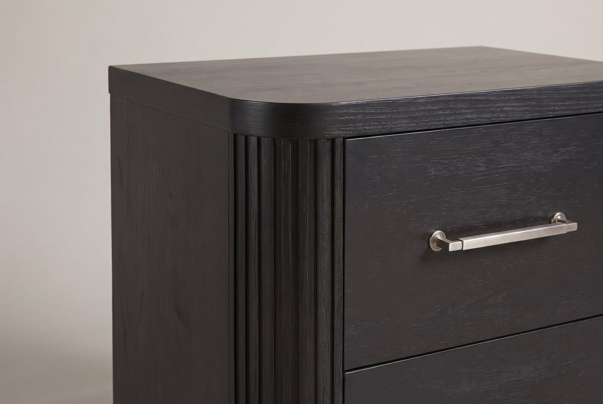 The front corner of the Bosa nightstand: reeded rounded column, rounded top corner and a metal bar pull on the top drawer