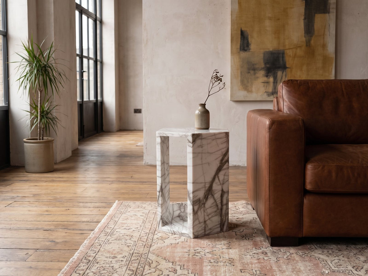 Bovino White Marble Hexagon Side Table beside a leather sofa in an industrial loft