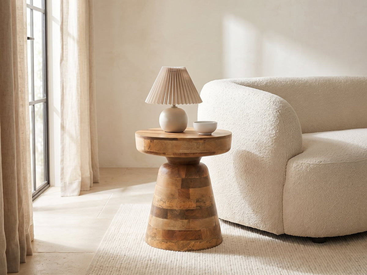 Bronte Solid Mango Pedestal Side Table with a lamp and a ceramic bowl beside a cream boucle armchair in a bright plaster room