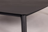 Close-up of the Brucoli table: the rounded corner of the solid aluminum top, the rail and the top of a tapered leg in matte black