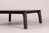 Two tapered black aluminum legs of the Brucoli coffee table at floor level, the rail under the thin top above