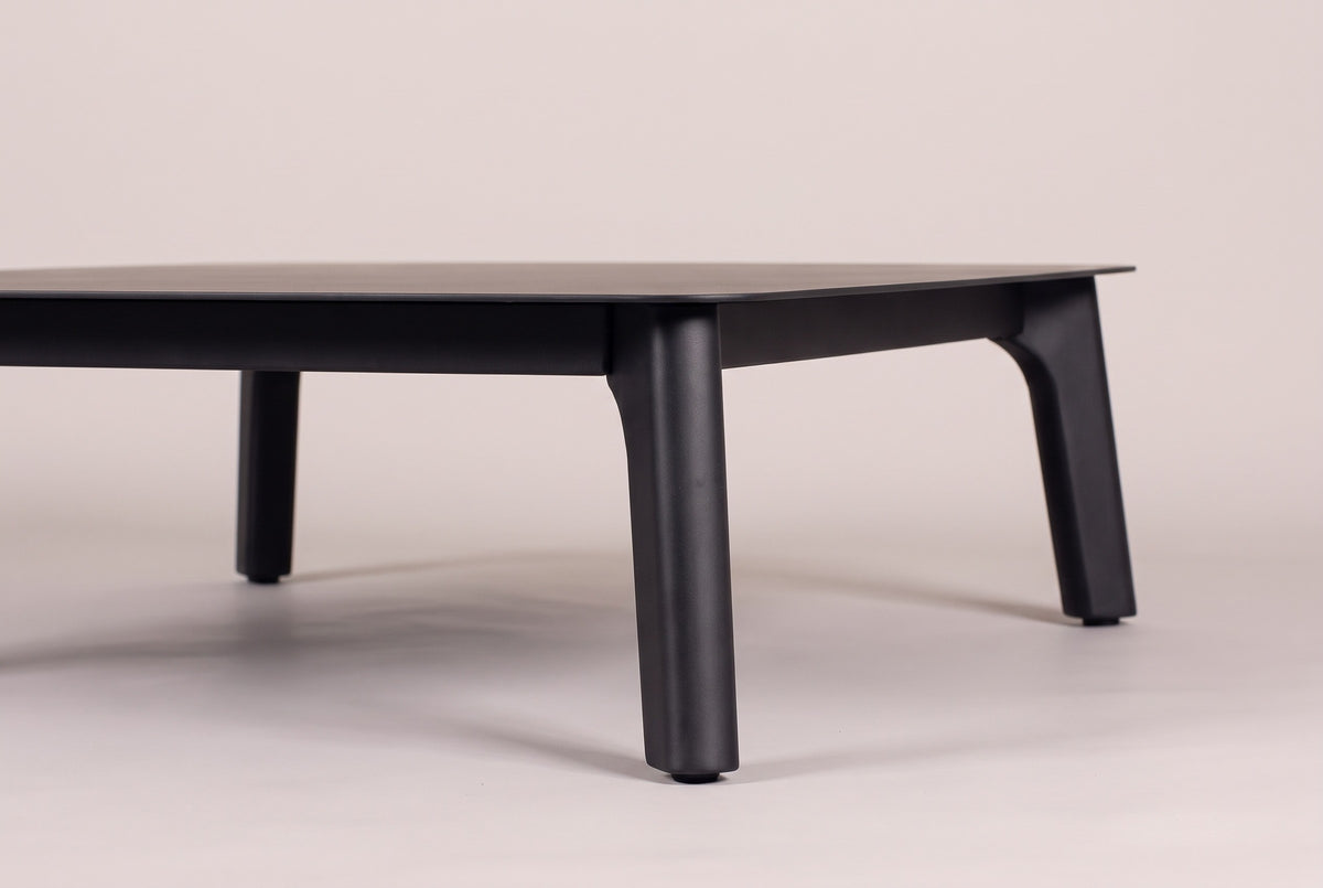 Two tapered black aluminum legs of the Brucoli coffee table at floor level, the rail under the thin top above