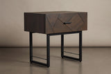 The Budoni one-drawer nightstand in smoked brown oak with an angled inlay front, a black bar pull and a black steel sled base, three-quarter view on a light studio backdrop