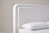 The upper corner of the Bussi headboard: the rounded corner, the raised boucle border and the plain inset panel above a white pillow