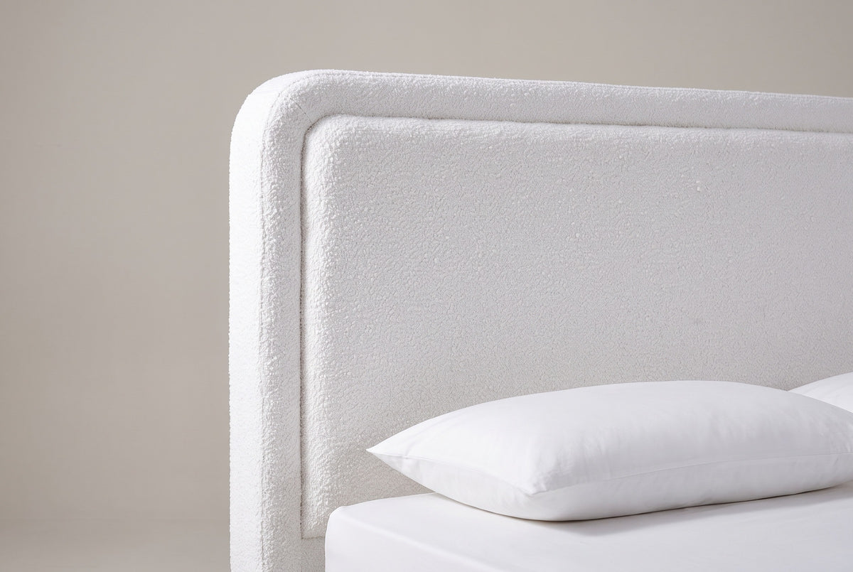 The upper corner of the Bussi headboard: the rounded corner, the raised boucle border and the plain inset panel above a white pillow