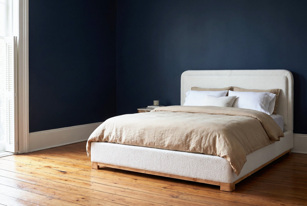Bussi white boucle bed against a deep navy wall in a New Orleans cottage bedroom, white shutters at the left