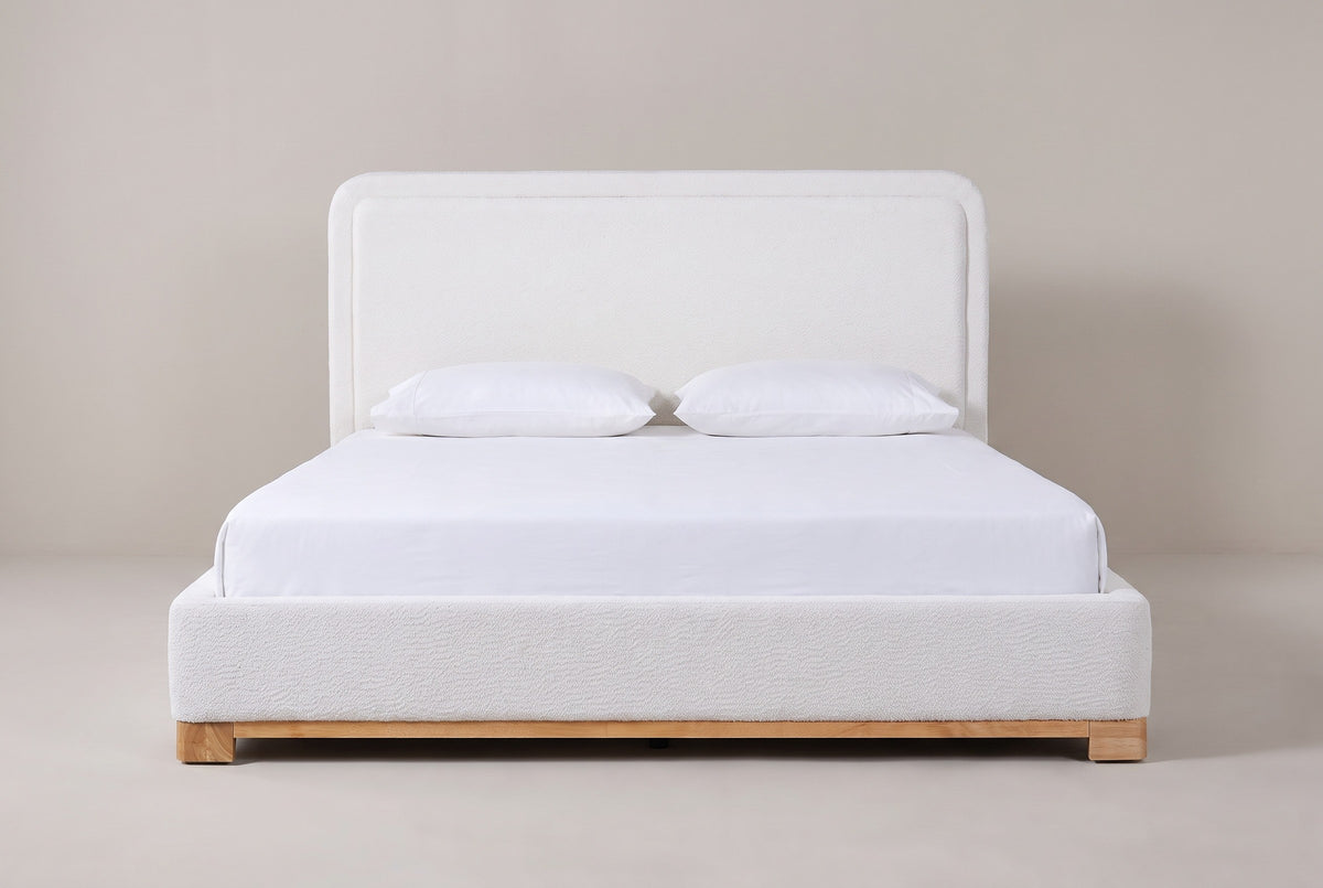 Bussi bed in white boucle on a light wood plinth with a white mattress and pillows (not included), front view